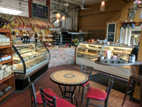 Cozy bakery interior with display cases, a round table, and chairs, featuring baked goods and a warm atmosphere.