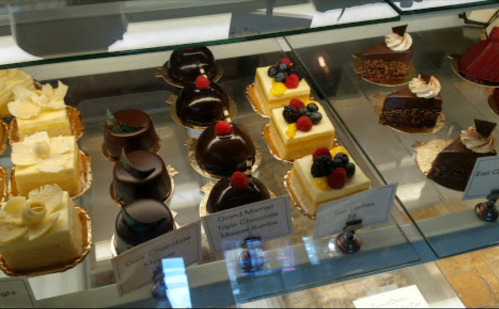 A display of assorted desserts, including chocolate mousse, fruit-topped cakes, and creamy pastries in a bakery case.