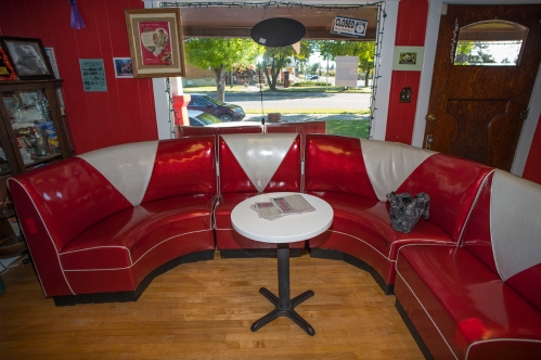 A cozy diner-style seating area with a red and white curved couch and a small round table in a bright room.