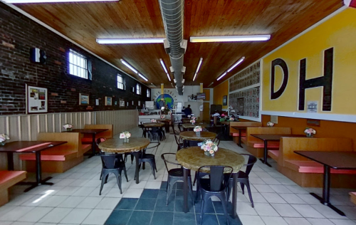Interior of a cozy restaurant with wooden accents, tables, and a counter in the background. Brightly colored walls.