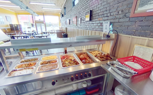 A buffet display with various dishes in a casual dining setting, featuring a brick wall and tables in the background.
