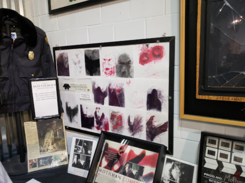 Display featuring Mothman artifacts, including sketches, photographs, and a police jacket, in a museum setting.