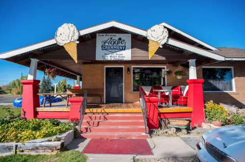 A charming ice cream shop with a wooden porch, red accents, and ice cream cone decorations on a clear blue sky day.