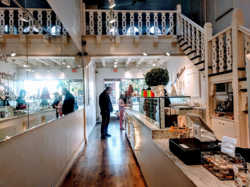 A bright, modern dessert shop with a staircase, featuring customers browsing and a display of treats.