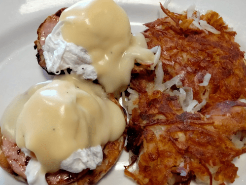 A plate featuring two eggs Benedict with hollandaise sauce and a side of crispy hash browns.