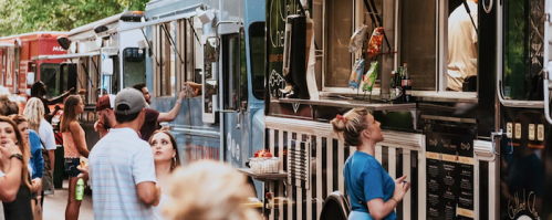 A lively food truck gathering with people ordering and enjoying food outdoors.