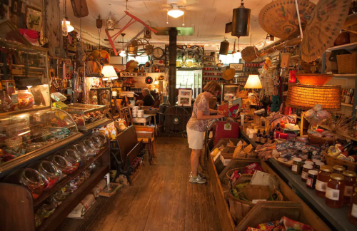 A cozy, cluttered antique shop filled with various vintage items, jars, and a customer browsing.