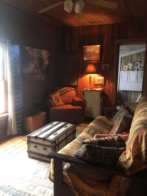 Cozy rustic living room with a wooden ceiling, a red armchair, a trunk, and warm lighting from a lamp.