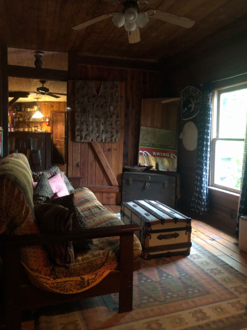 Cozy rustic living room with wooden walls, a patterned rug, a vintage trunk, and a comfortable sofa.