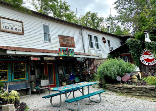 A rustic building with colorful signs, a tasting room, and a picnic table surrounded by greenery.