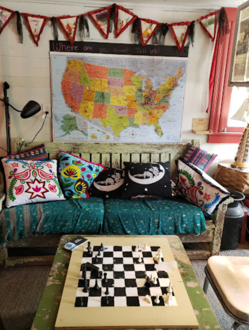 Cozy seating area with colorful pillows, a chessboard, and a map of the USA on the wall, decorated with flags.