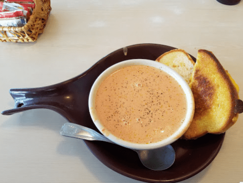 A bowl of creamy soup with a sprinkle of pepper, served with two slices of toasted bread on a brown plate.
