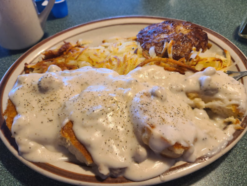 A plate of biscuits smothered in creamy gravy, served with hash browns and a sausage patty.