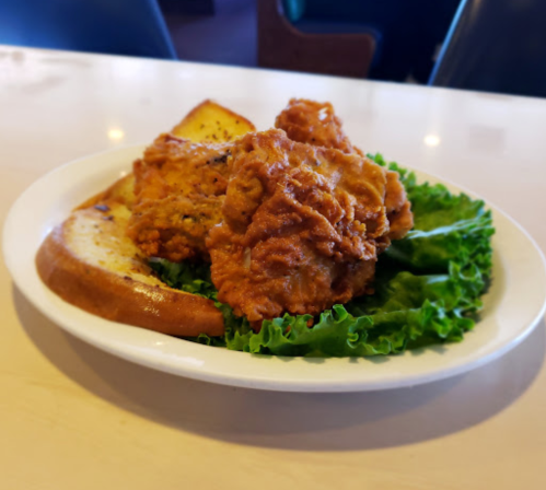A plate of crispy fried chicken on a bed of lettuce, accompanied by a slice of bread.