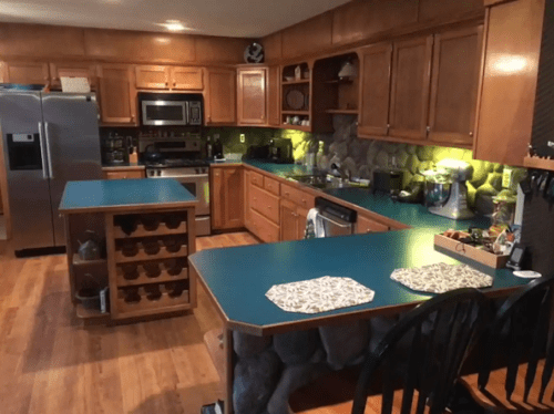 A spacious kitchen with wooden cabinets, teal countertops, stainless steel appliances, and a central island.