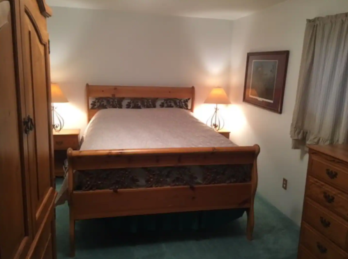 Cozy bedroom featuring a wooden bed, nightstands with lamps, and a dresser, all on green carpet.