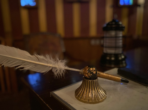 A decorative inkwell with a feather quill and pen, set on a wooden table in a dimly lit room.