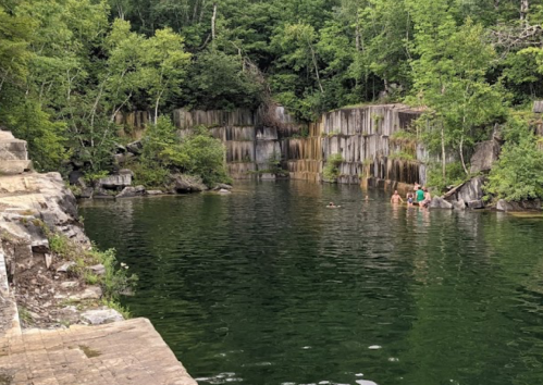 A serene swimming area surrounded by rocky cliffs and lush greenery, with people enjoying the water.
