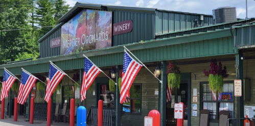 A green building with a sign for "Wenger Orchards Winery," featuring American flags and hanging plants outside.