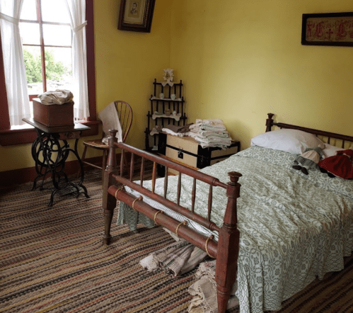 A cozy bedroom with a wooden bed, patterned bedding, a chair, and a small table, featuring warm yellow walls.