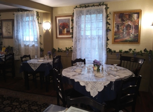 Cozy restaurant interior with lace tablecloths, wooden chairs, and decorative paintings on the walls. Soft lighting.