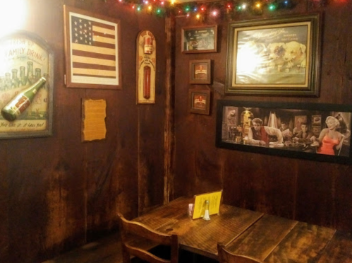 Cozy restaurant corner with wooden walls, vintage decor, an American flag, and colorful string lights.