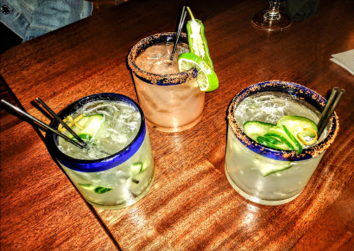 Three colorful cocktails with garnishes, served in rimmed glasses on a wooden table.