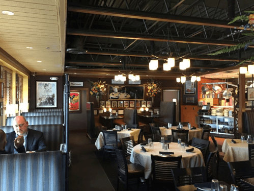 A cozy restaurant interior with tables, chairs, and decorative elements, featuring a man in a suit in the foreground.