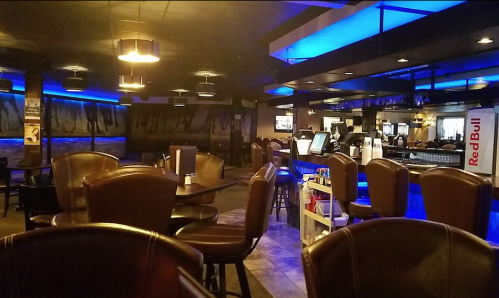 Interior of a dimly lit bar with blue lighting, empty tables, and a long bar counter in the background.