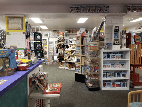 A colorful store interior filled with shelves of toys, games, and stuffed animals, with a display counter in the foreground.
