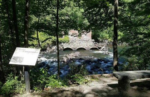 A stone structure over a river, surrounded by trees, with an informational sign nearby.