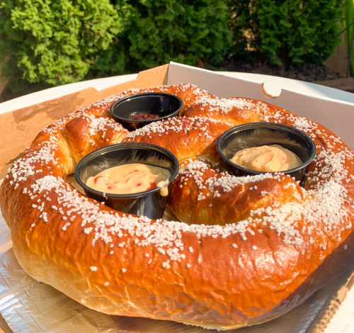 A large, soft pretzel with coarse salt, served in a box with three dipping sauces.