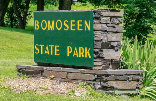Sign for Bomoseen State Park, featuring green background and yellow lettering, surrounded by grass and trees.