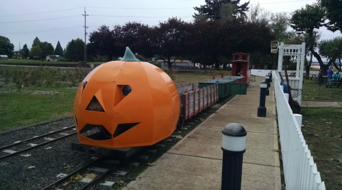 A train car designed as a large orange pumpkin, sitting on tracks in a park setting.