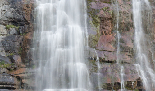 A cascading waterfall flows over rocky cliffs, surrounded by lush greenery.