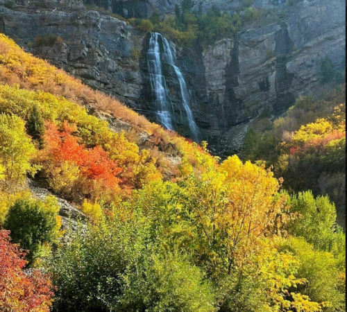 A scenic view of a waterfall cascading down rocky cliffs, surrounded by vibrant autumn foliage in shades of orange and yellow.