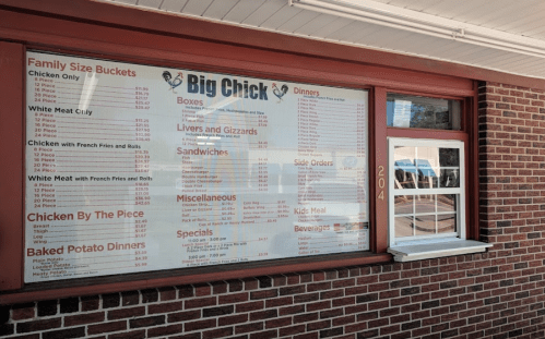 Menu board for Big Chick featuring various chicken dishes, sides, and prices displayed on a brick wall.