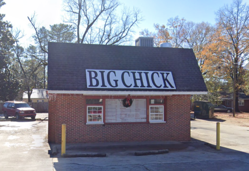 A small brick building with a large sign reading "BIG CHICK," surrounded by trees and parked cars.