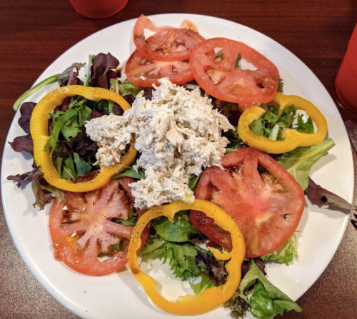 A colorful salad with mixed greens, sliced tomatoes, yellow bell peppers, and shredded chicken on top.