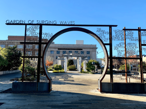 Entrance to the Garden of Surging Waves, featuring a decorative arch and landscaped greenery under a clear blue sky.