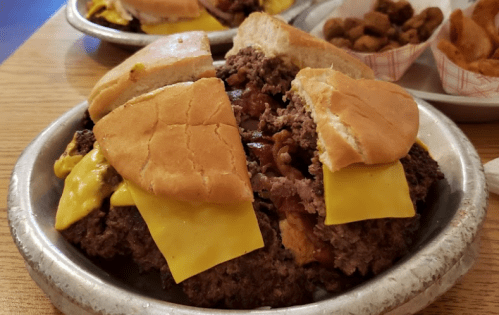 A large cheeseburger with two patties, melted cheese, and split buns, served on a silver plate.