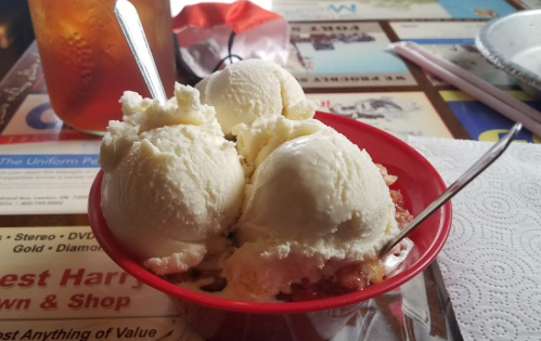 A red bowl filled with three scoops of vanilla ice cream, sitting on a table with a menu and a drink in the background.