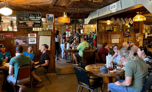 A bustling restaurant interior with diners at tables, wooden decor, and a lively atmosphere.