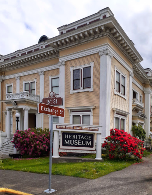 Historic building with a sign for the Heritage Museum, surrounded by colorful flowers and greenery.