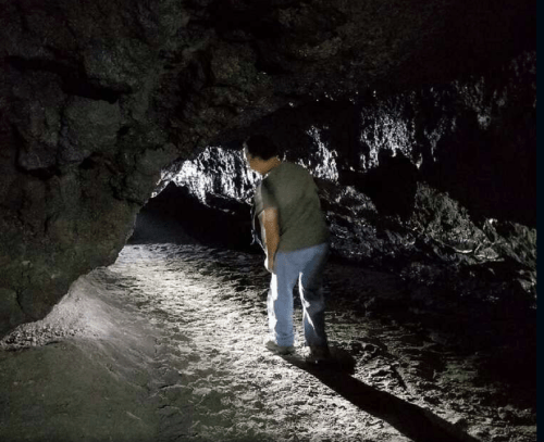 A person stands in a dark cave, illuminated by a flashlight, exploring the rocky interior.