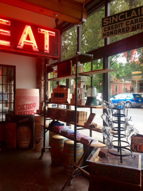 A cozy shop interior featuring vintage decor, shelves with products, and a bright "EAT" neon sign.
