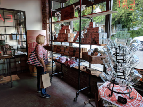 A person browses products on shelves in a cozy store with large windows and a variety of displayed items.