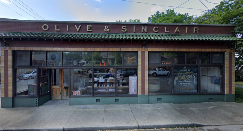 Exterior of Olive & Sinclair store, featuring a brick facade, large windows, and an "OPEN" sign.