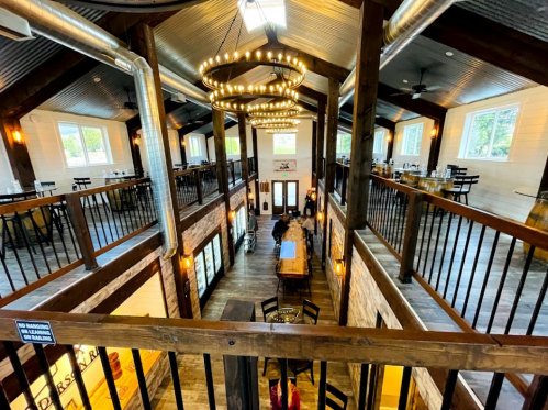 Interior of a spacious restaurant with high ceilings, wooden beams, and a large central dining area illuminated by chandeliers.