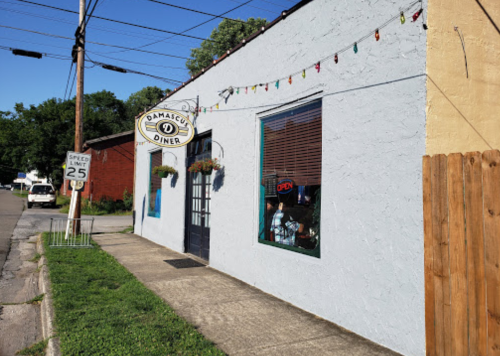A colorful diner with a sign reading "Open," located on a quiet street with decorative lights and a wooden fence.